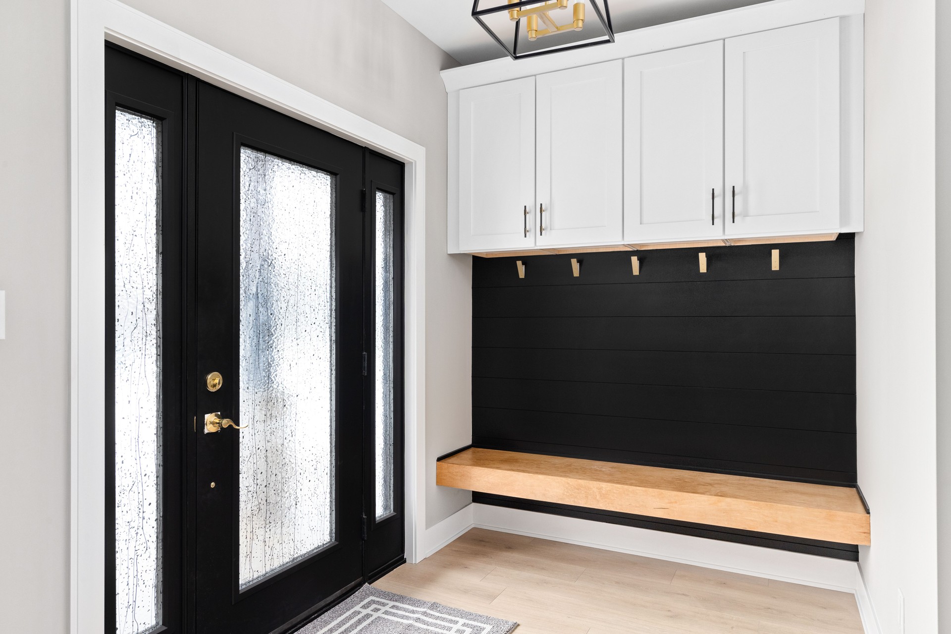An entryway with a black door and shiplap, white cabinets, and a wooden bench.